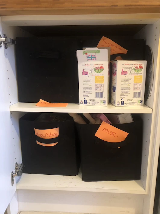 White kitchen cupboard with two shelves full of black cube storage boxes