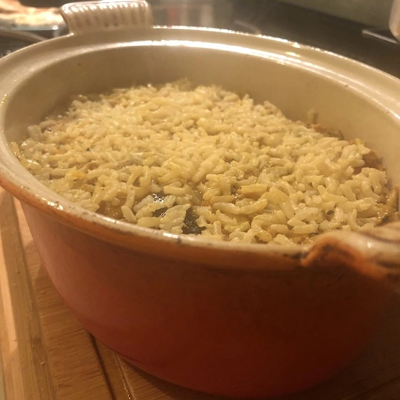 Red casserole dish containing biryani with only rice layer visible